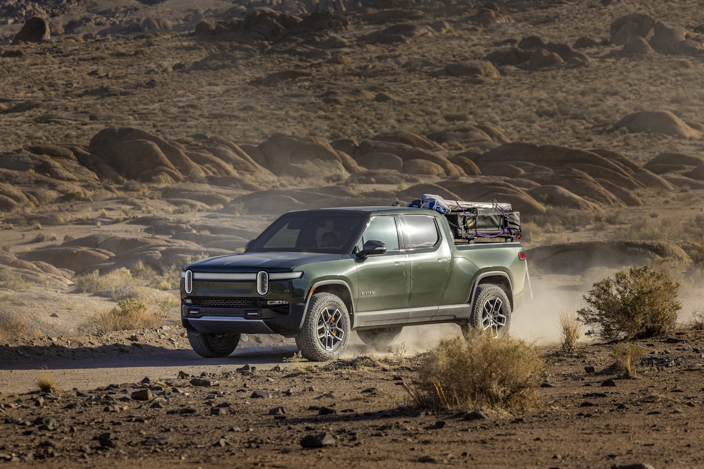 Green Rivian R1T electric truck driving on a dirt road through the Alabama Hills